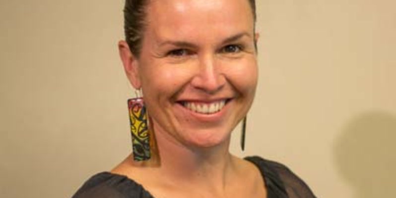 freelance science communicator Kylie Bailey - head and shoulders smiling at camera wearing dark top and bright earrings with hair tied back