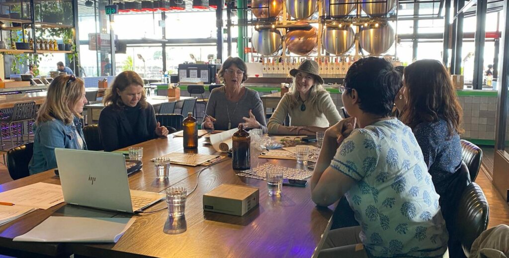 Image of GoodSense team members around a large table - seated Left to right Allanah Robinson, Kylie Bailey, Jo Patterson, Kath Dewar, Kate Jamieson, Karen Short, Moumita Das Roy