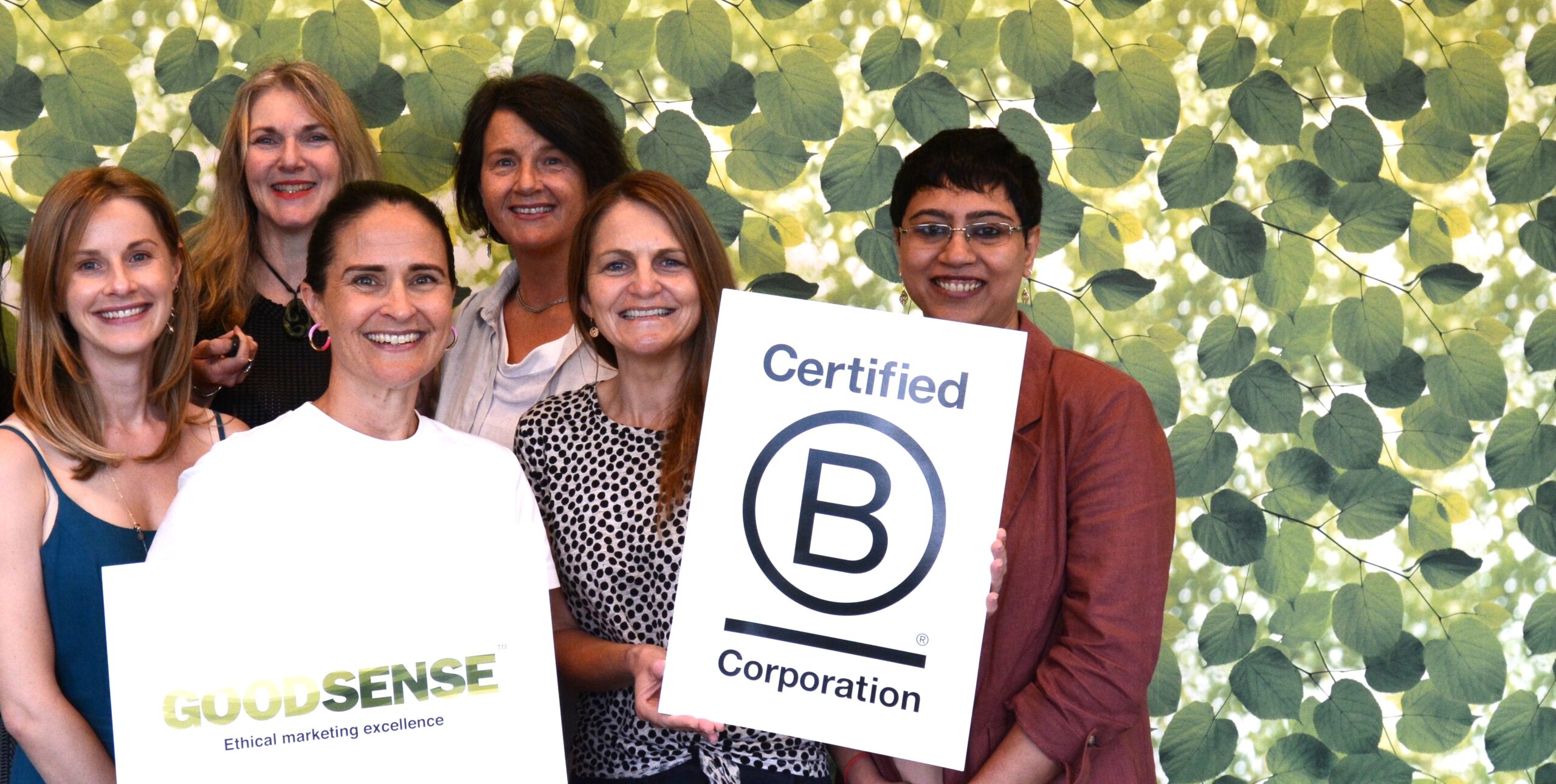 GoodSense B Corp certified marketing team smiling at camera against a leafy background