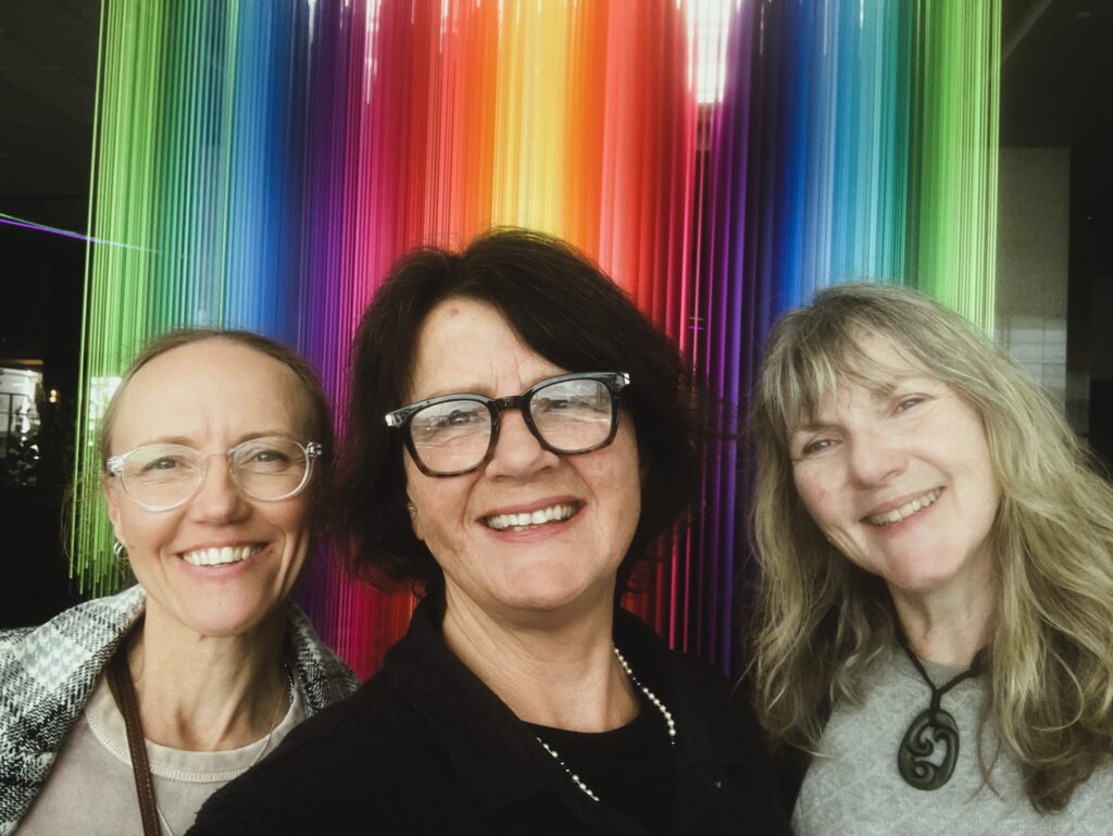 GoodSense team members Lani Dodds Jo Patterson and Katherine Dewar infront of rainbow lights symbolising inclusion